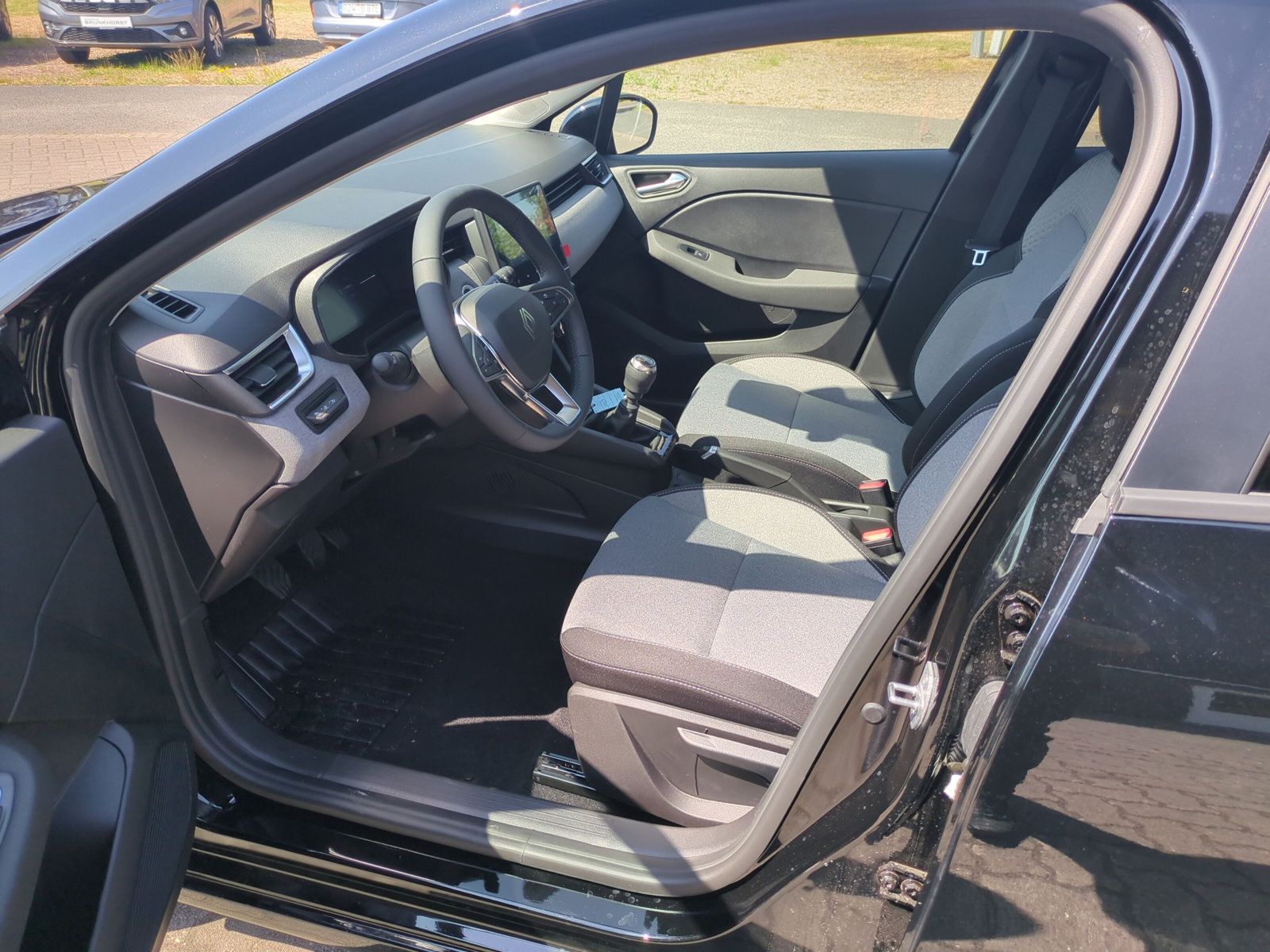 Renault Clio Innenraum mit grau-schwarzen Stoffsitzen, Lenkrad mit Markenlogo, Schaltgetriebe und modernem Armaturenbrett in einem Autohaus