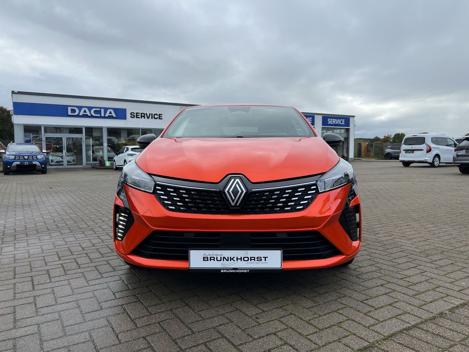 Orangefarbener Renault Clio Neuwagen in modernem Autohaus Brunkhorst Showroom mit großen Fensterfronten und eleganter Sitzecke
