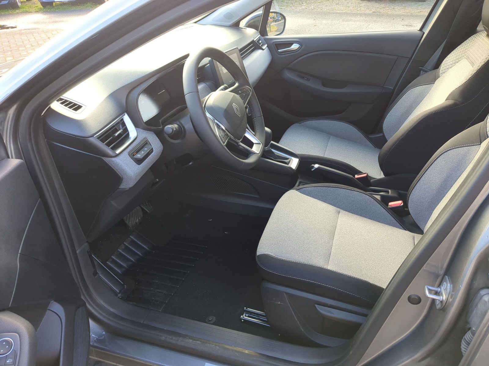 Innenansicht Renault Clio Fahrertür offen mit schwarzem Armaturenbrett, grauem Stoffsitz und Lenkrad im Autohaus Showroom