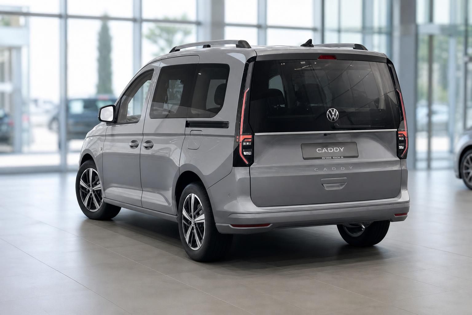 VW Caddy in Grau, Heckansicht im Autohaus mit Panoramaverglasung