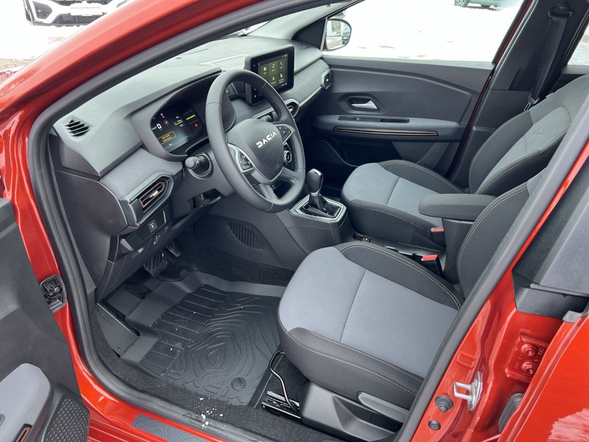 Dacia Innenraum Fahrerseite mit Lenkrad, digitalem Cockpit und grauen Stoffsitzen in rotem Fahrzeug