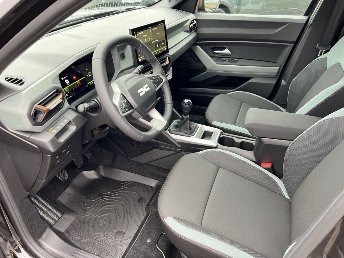 Dacia Innenraum mit Lenkrad, Digitalinstrumenten, Schaltgetriebe und grauen Stoffsitzen