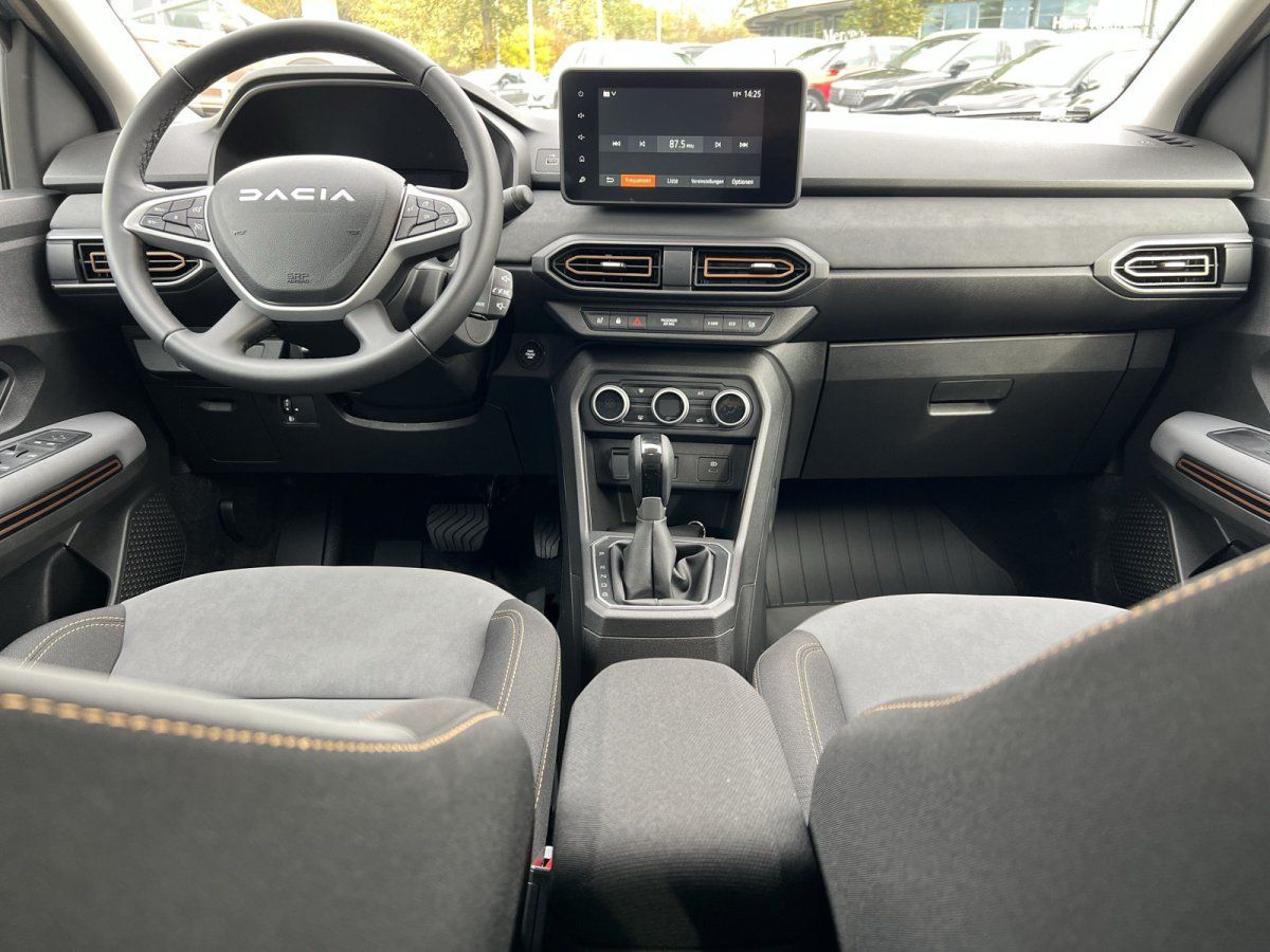 Dacia Innenraum mit Touchscreen, Lenkrad und manueller Schaltung in Grau mit orangefarbenen Akzenten