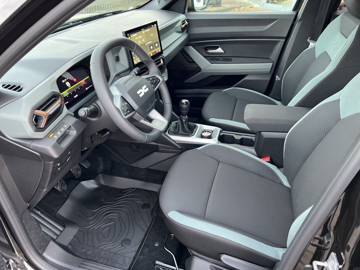 Dacia Innenraum mit Lenkrad, Touchscreen-Display, Stoffsitzen in Grau-Grün und Schaltgetriebe