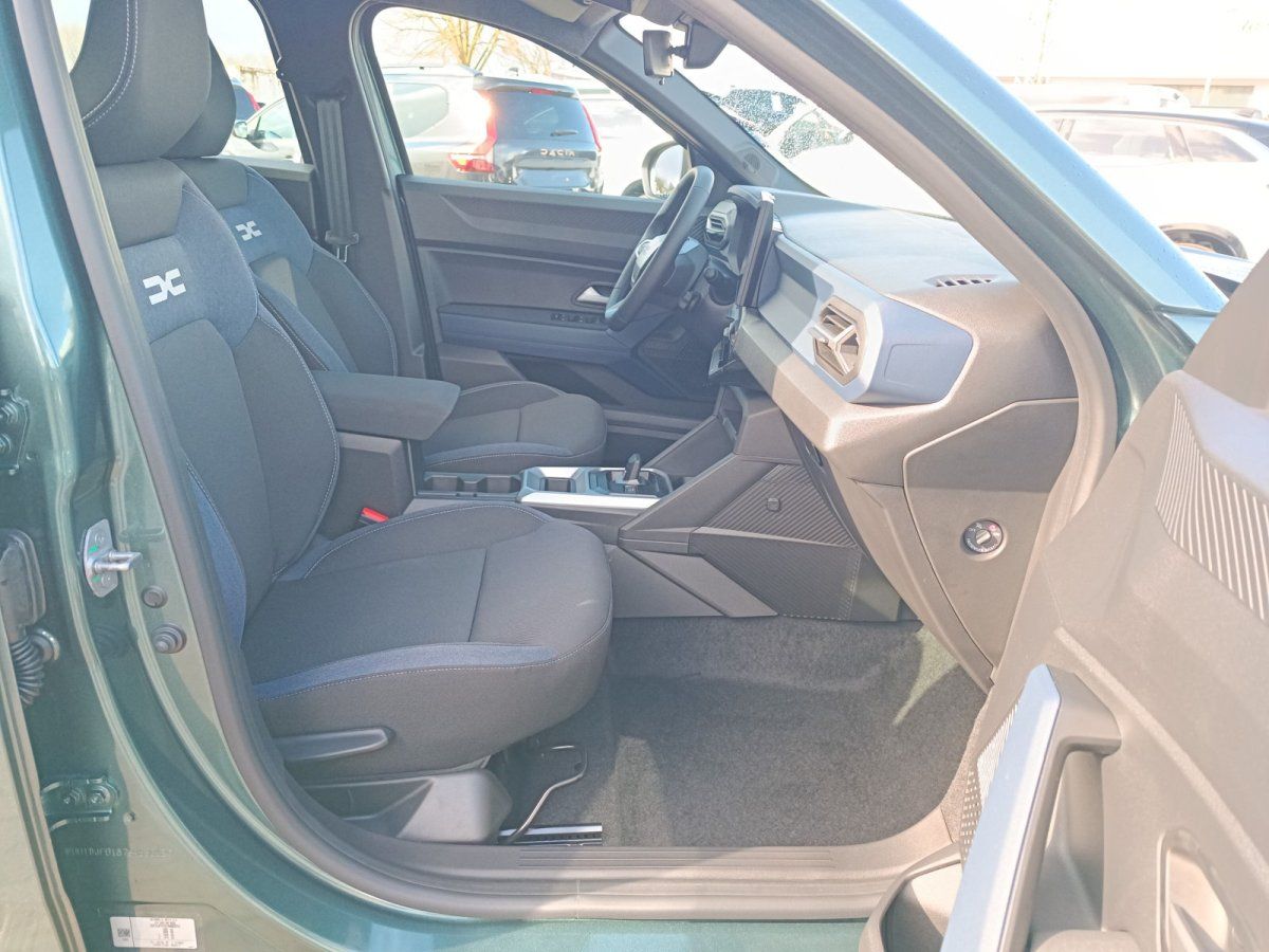 Dacia Innenraum mit schwarzen Stoffsitzen, Mittelkonsole und Cockpit in grünem SUV