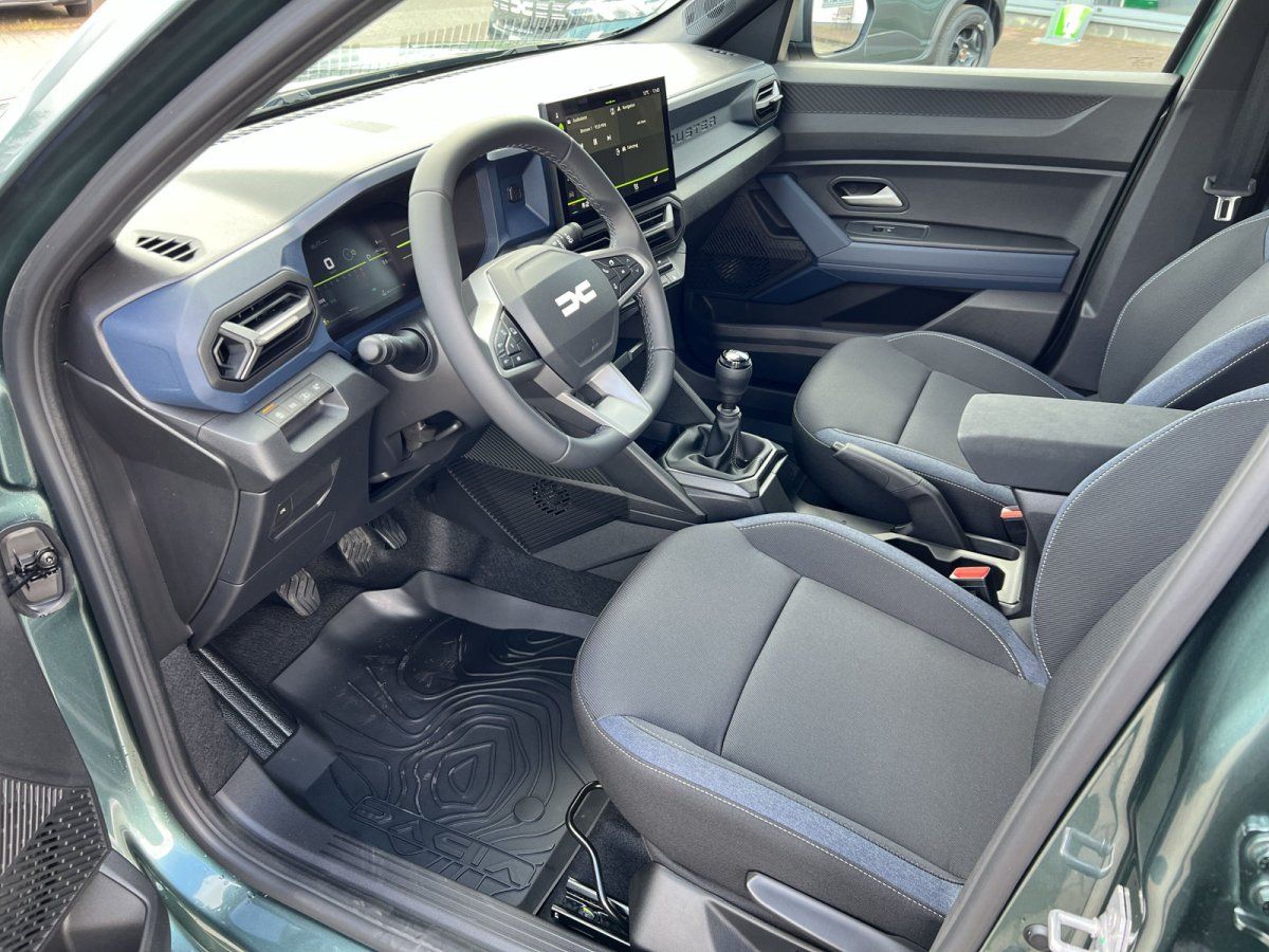 Dacia Innenraum mit Lenkrad, Infotainment-Display und Schaltgetriebe in grauem Stoffinterieur