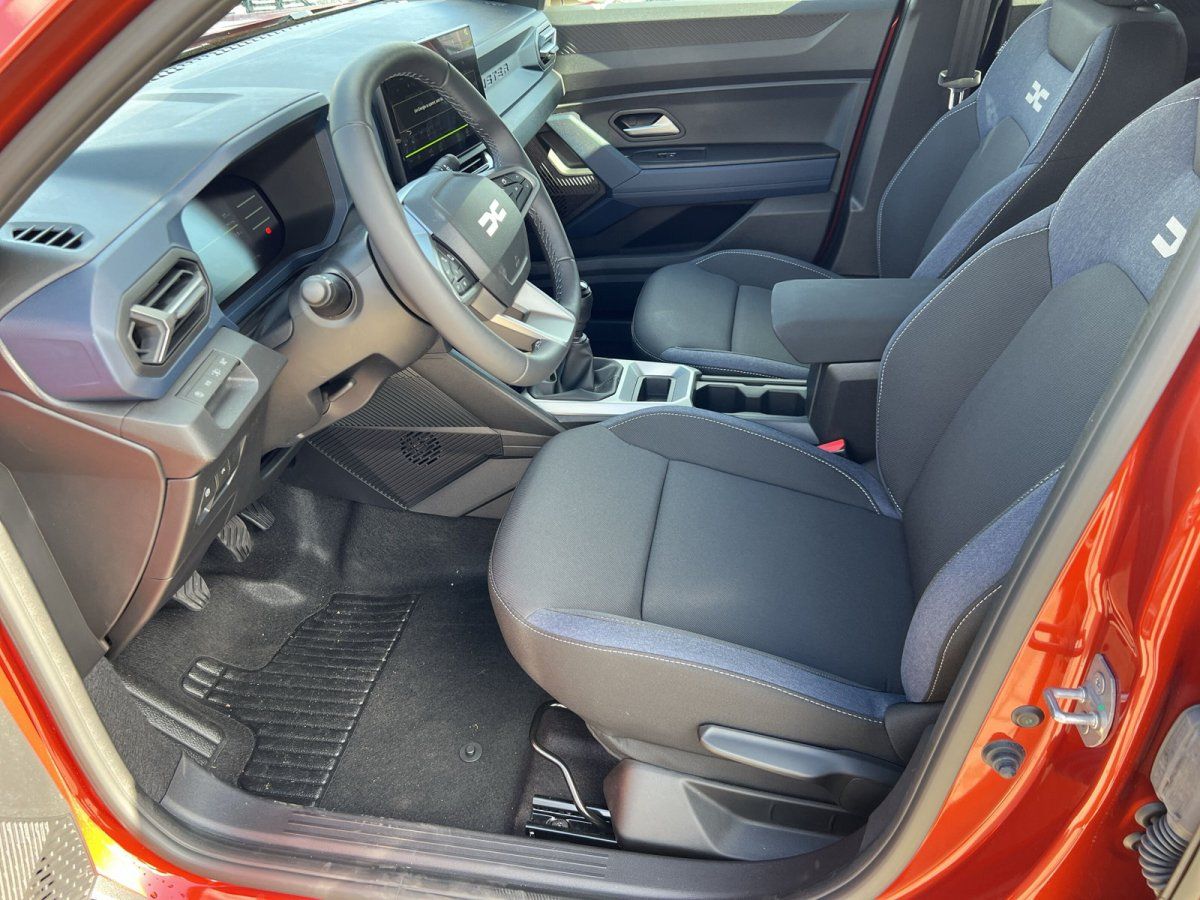 Dacia Innenraum Fahrerseite mit dunklen Stoffsitzen und modernem Cockpit in orangenem Fahrzeug