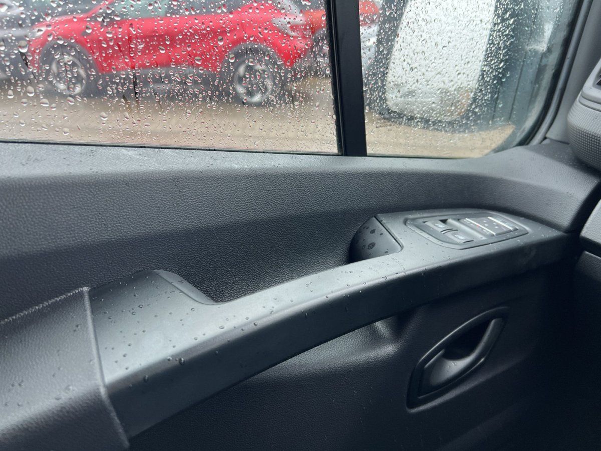 Fahrzeuginnenraum Türverkleidung mit Fensterheber-Schalter, im Hintergrund VW-Autohaus mit mehreren Fahrzeugen