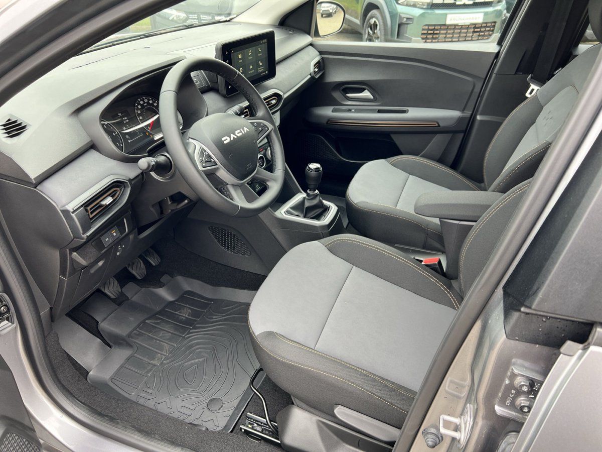 Dacia Innenraum mit Lenkrad, Touchscreen-Display, Schaltgetriebe und grauen Stoffsitzen