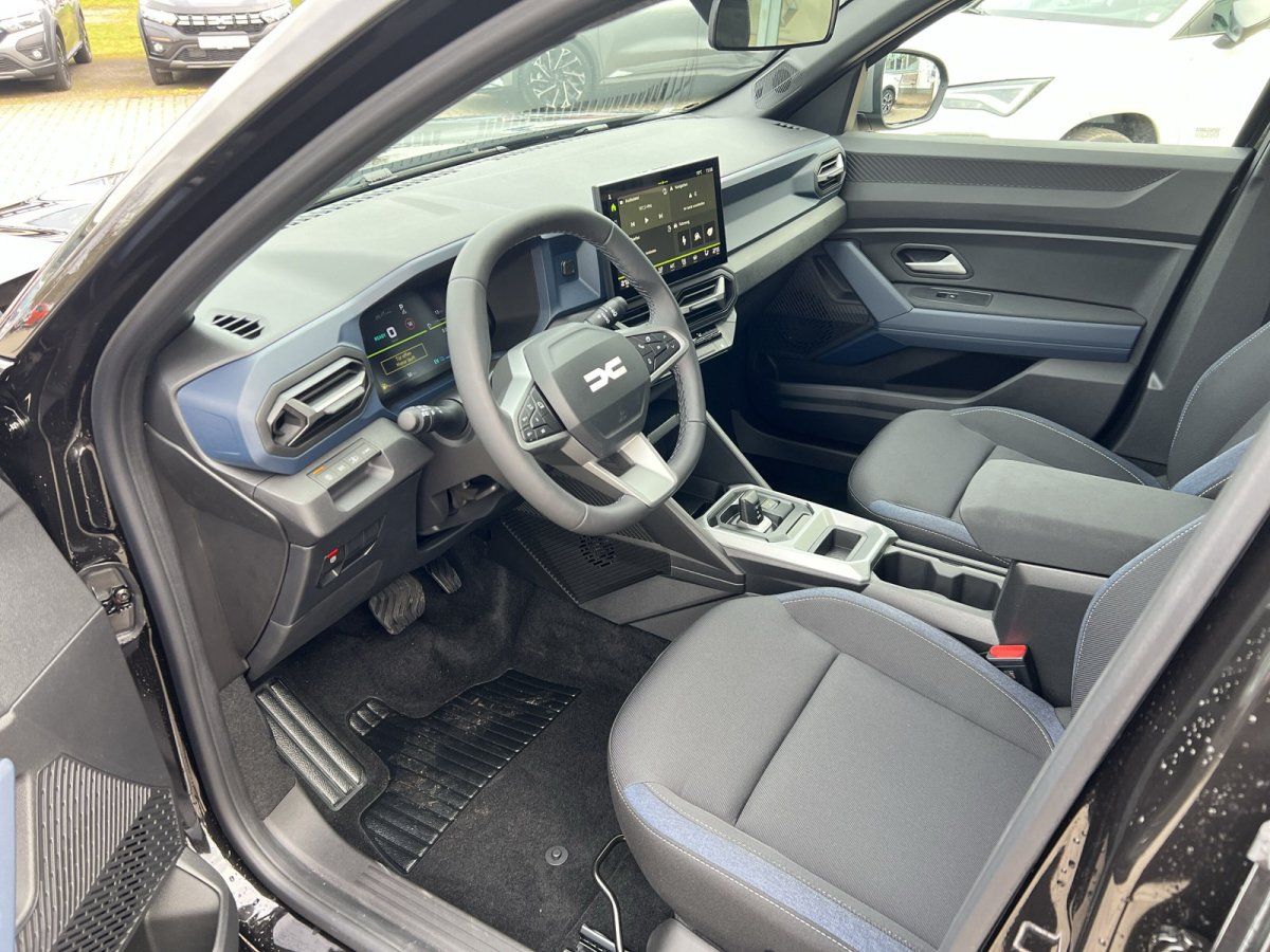 Moderner Innenraum eines Dacia Fahrzeugs mit Touchscreen, Lenkrad und grauen Sitzen