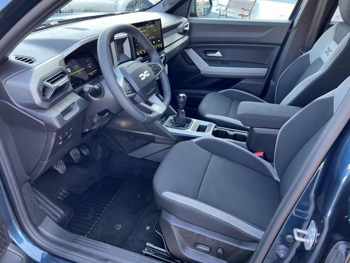 Dacia Innenraum mit Lenkrad, Infotainment-Display, Schalthebel und schwarzen Stoffsitzen