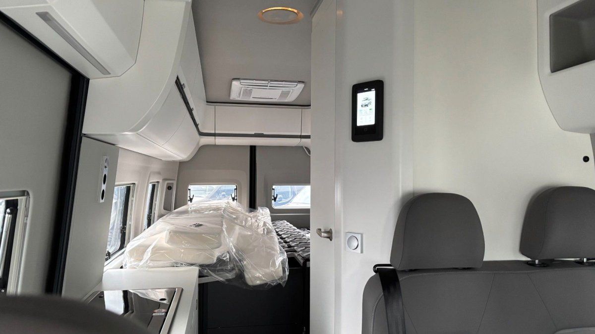 Modernes Wohnmobil Innenraum mit weißen Wänden, grauem Fahrersitz und digitalem Bedienpanel