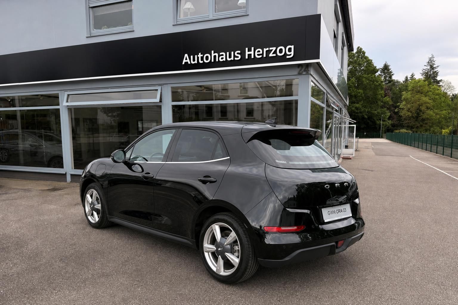Schwarzer ORA 03 E-Auto von hinten links - elegante Schrägheckform mit sportlichen Felgen und Ladeanschluss