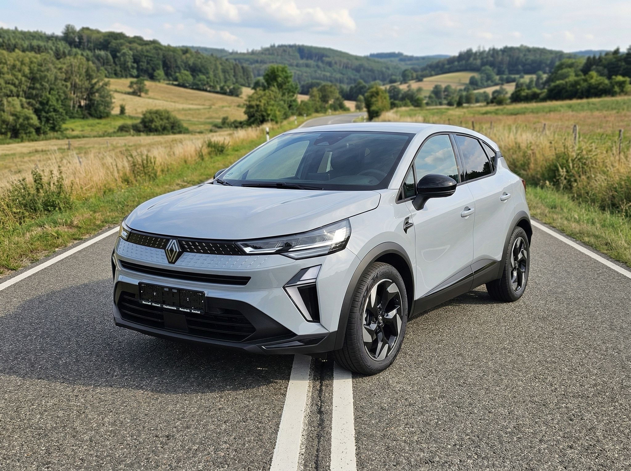 Renault Captur silber SUV Frontansicht auf Landstraße mit Hügellandschaft im Hintergrund