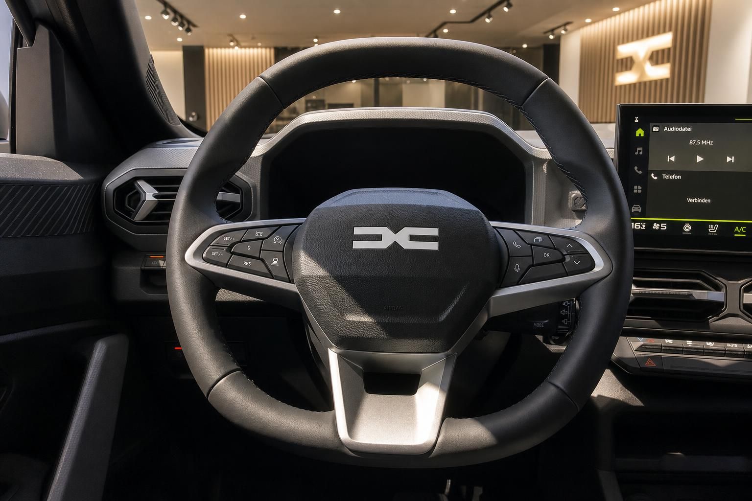 Dacia Lenkrad mit Logo und Multifunktionstasten sowie Touchscreen-Infotainment im Hintergrund