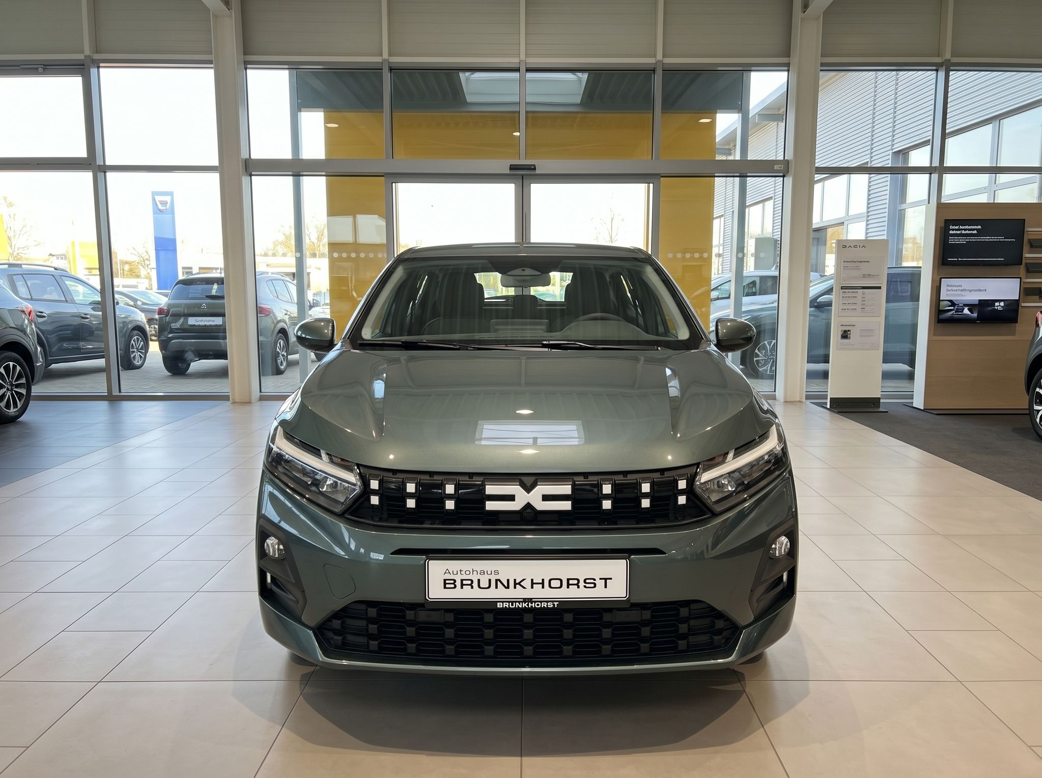 Dacia Sandero grün metallic Frontansicht mit Dacia Logo im Autohaus Showroom