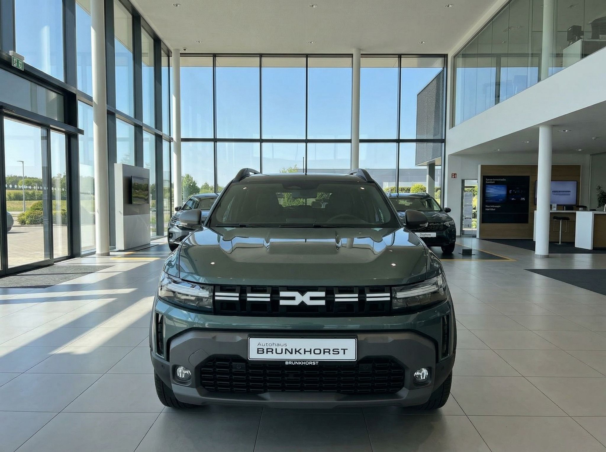 Dacia SUV Frontansicht graugrün mit BRUNKHOSRT Kennzeichen im modernen Autohaus