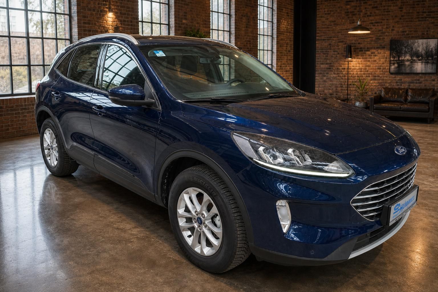 Ford Kuga blau, Frontansicht schraeg vor Backsteinwand im Showroom