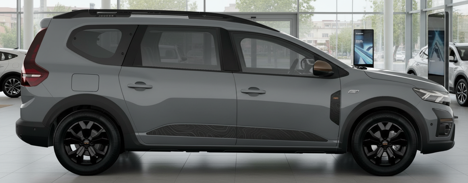Grauer Dacia Jogger Seitenansicht im Autohaus mit schwarzen Felgen und Topografie-Dekor