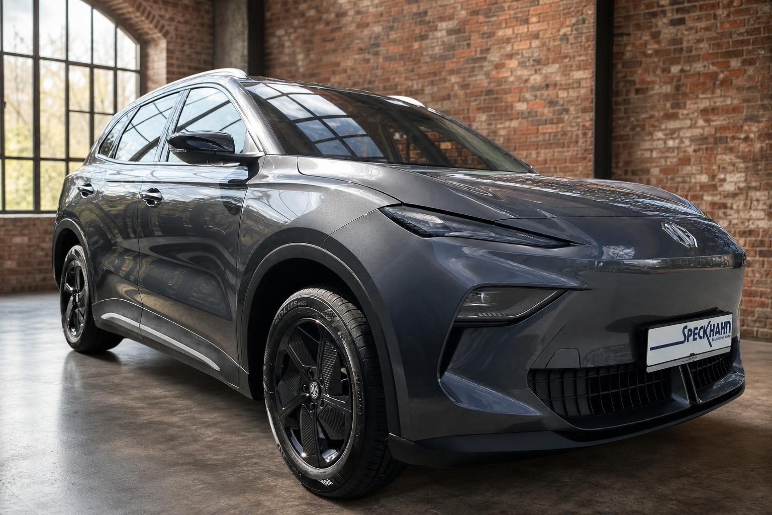 MG SUV Grau, Frontansicht seitlich mit Felgen vor Backsteinwand