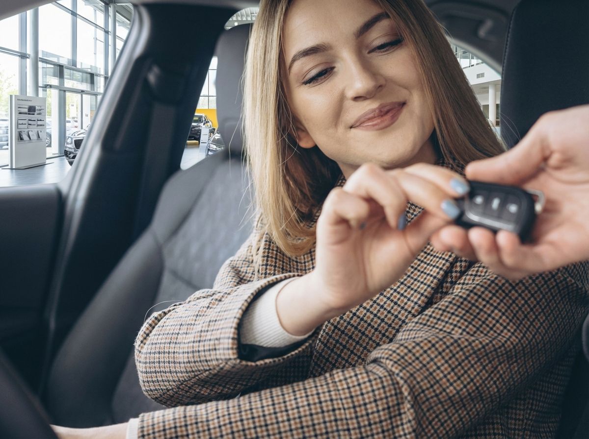 Frau erhält Autoschlüssel im Autohaus – Fahrzeugübergabe im Innenraum
