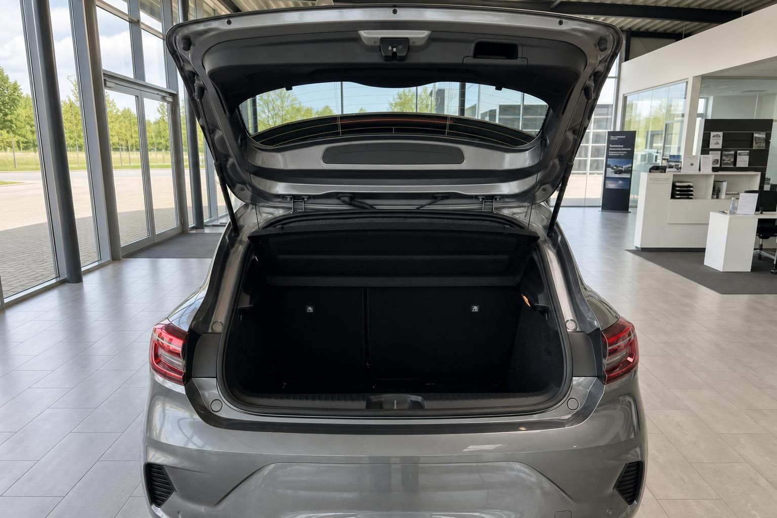 Geöffneter Kofferraum eines grauen Fahrzeugs im Autohaus-Showroom mit schwarzer Innenausstattung