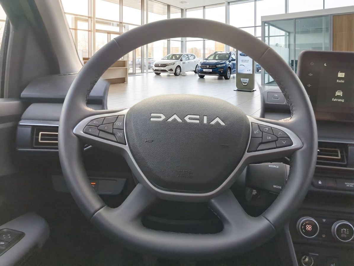 Dacia Lenkrad mit Multifunktionstasten und Blick ins Autohaus mit weiteren Fahrzeugen