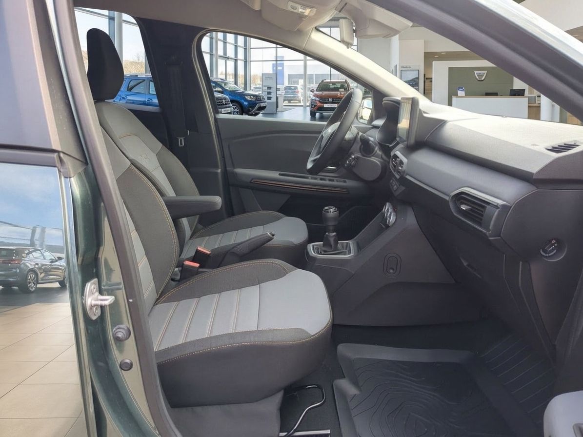 Dacia Fahrzeuginnenraum mit grauen Sitzen, Schaltgetriebe und geöffneter Beifahrertür