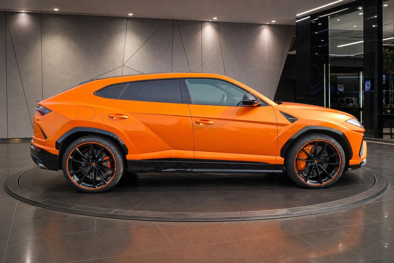 Lamborghini Urus orange Seitenansicht links im Showroom – SUV mit schwarzen Sportfelgen