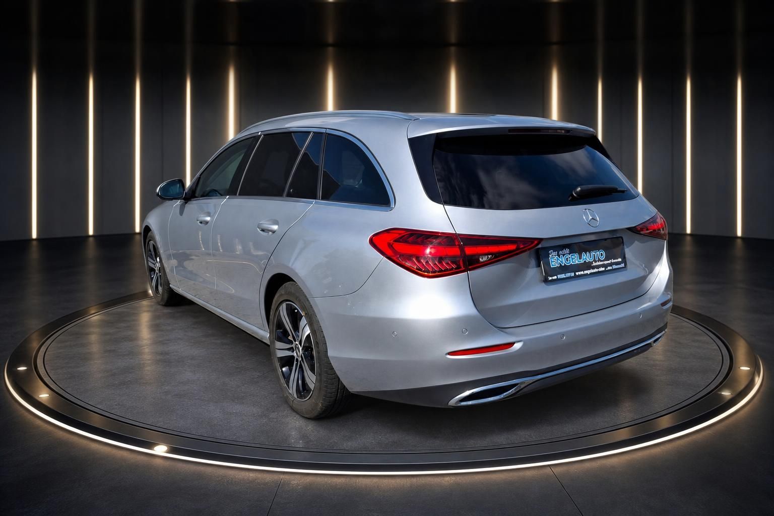 Silberner Mercedes-Benz Kombi Heckansicht mit Engelauto Kennzeichenrahmen im Showroom