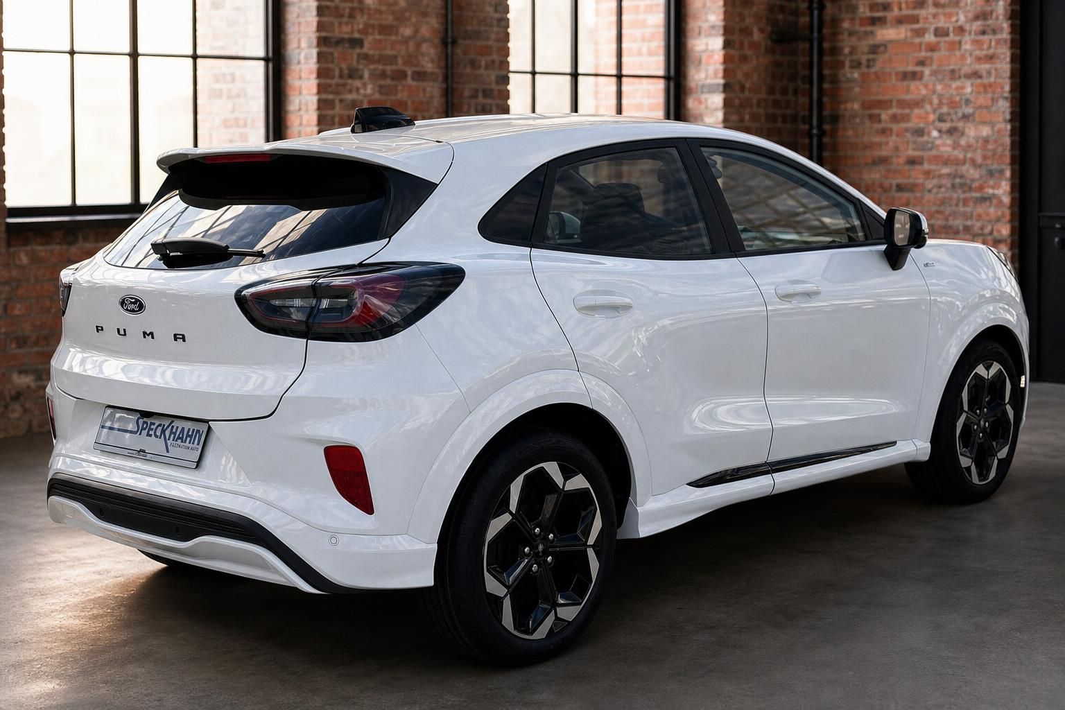 Ford Puma weiss Heckansicht schraeg vor Backsteinwand im Showroom
