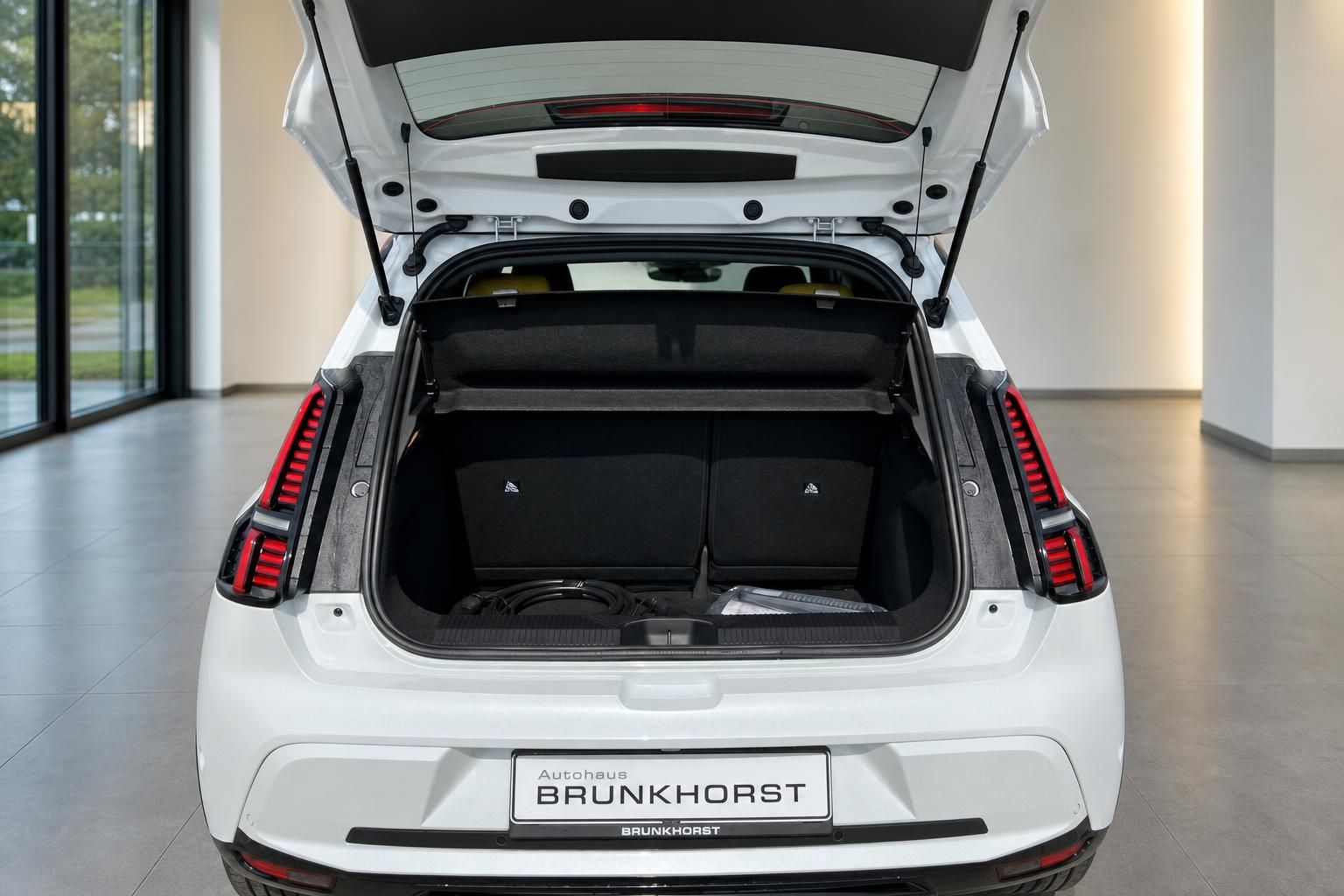 Geoeffneter Kofferraum eines weissen Elektroautos mit Ladekabel im Showroom