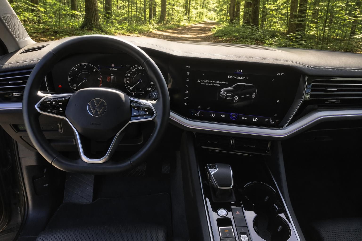 Volkswagen Innenraum mit modernem Cockpit, Touchscreen und Lenkrad - Blick durch Windschutzscheibe auf Waldweg