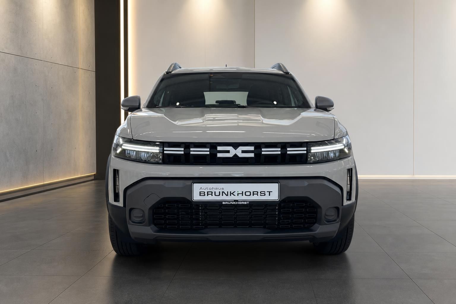 Dacia Duster SUV Frontansicht in grau mit schwarzem Kühlergrill im modernen Showroom