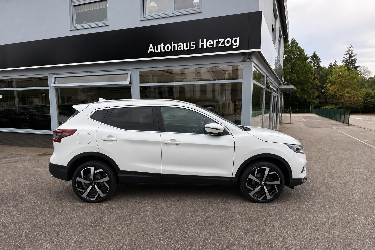 Weißer Nissan Qashqai Seitenansicht vor Autohaus Herzog