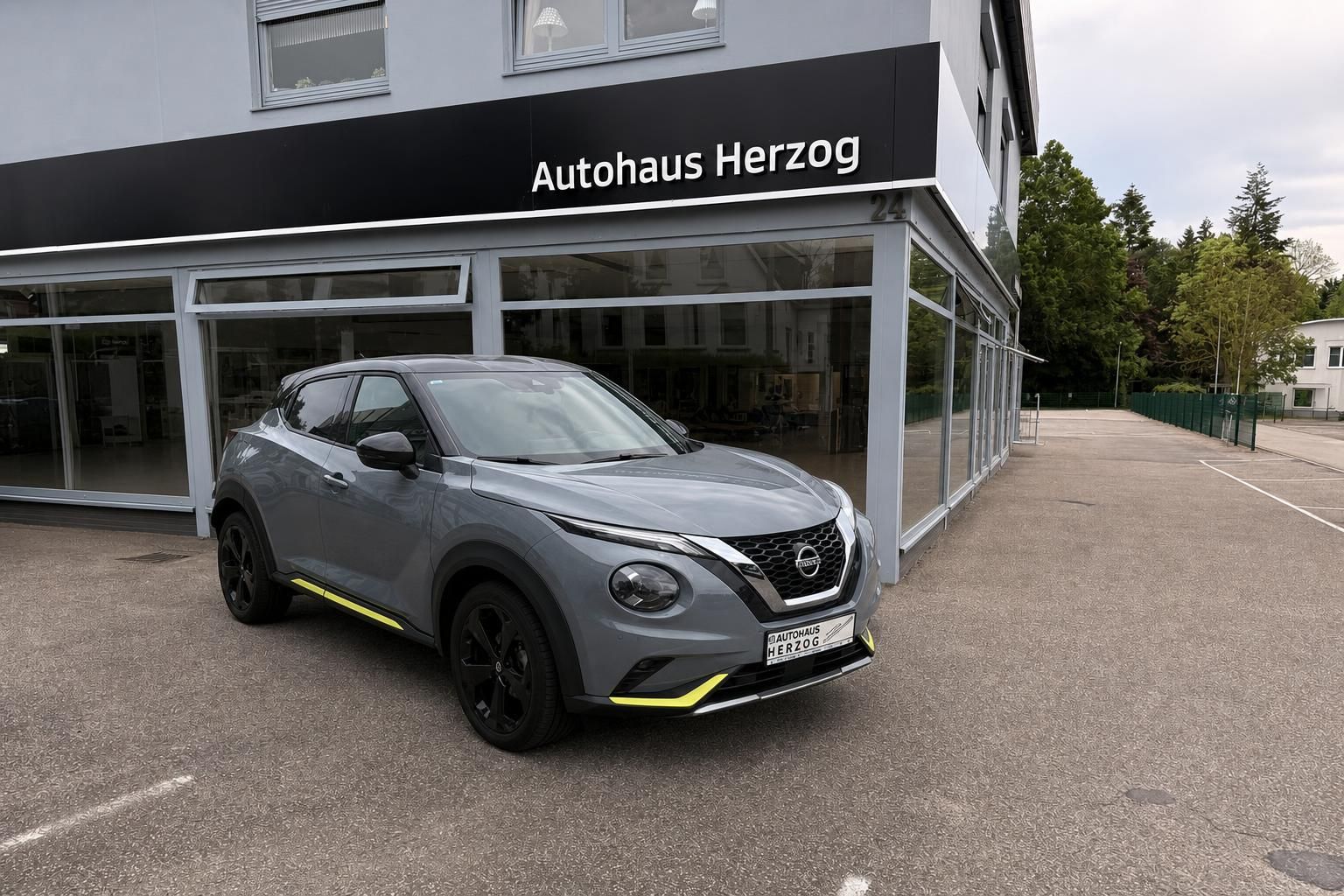 Nissan Juke grau metallic mit gelben Akzenten vor Autohaus - Frontansicht des Crossover SUV