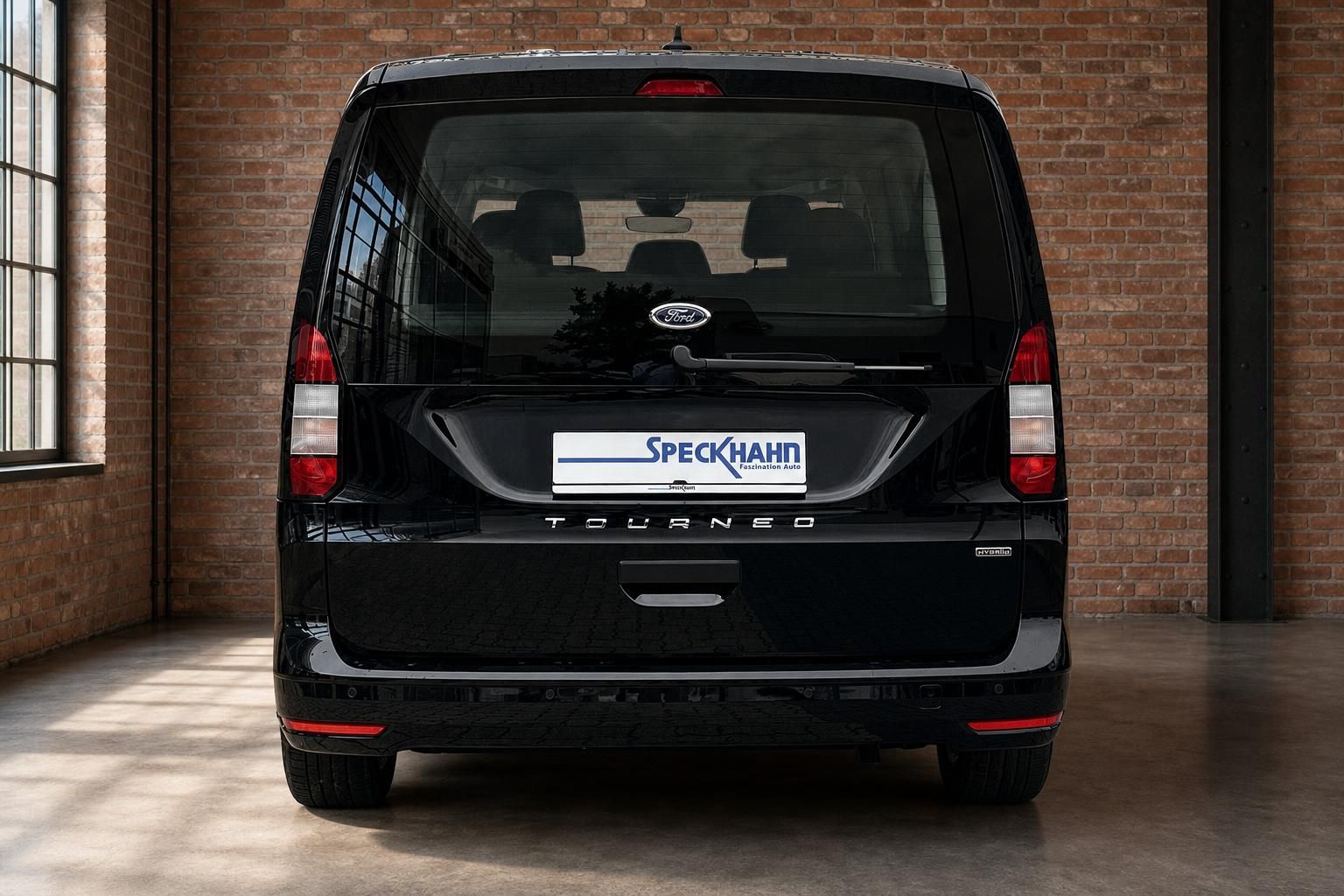 Ford Tourneo Hybrid schwarz, direkte Heckansicht vor Backsteinwand