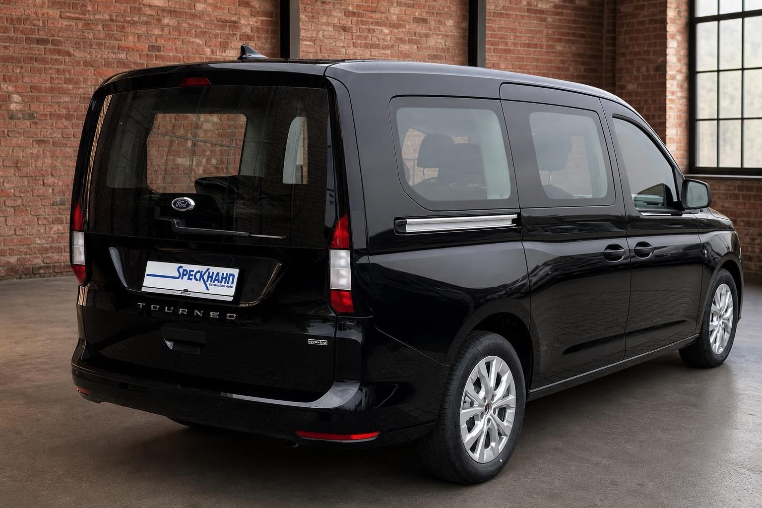 Ford Tourneo Hybrid schwarz, Heckansicht schraeg in Halle mit Backsteinmauer