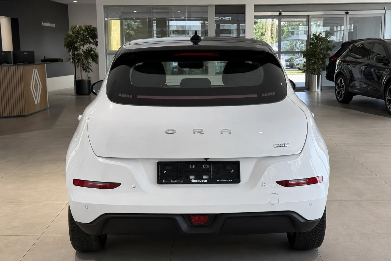 Weißer ORA Elektro-Kleinwagen, Heckansicht mit ORA-Schriftzug und Händlerkennzeichen im Showroom