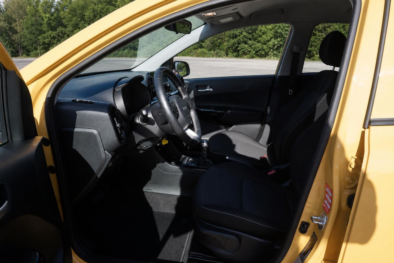 Kia Picanto Innenraum Fahrerseite mit Lenkrad, Schaltgetriebe und schwarzen Stoffsitzen