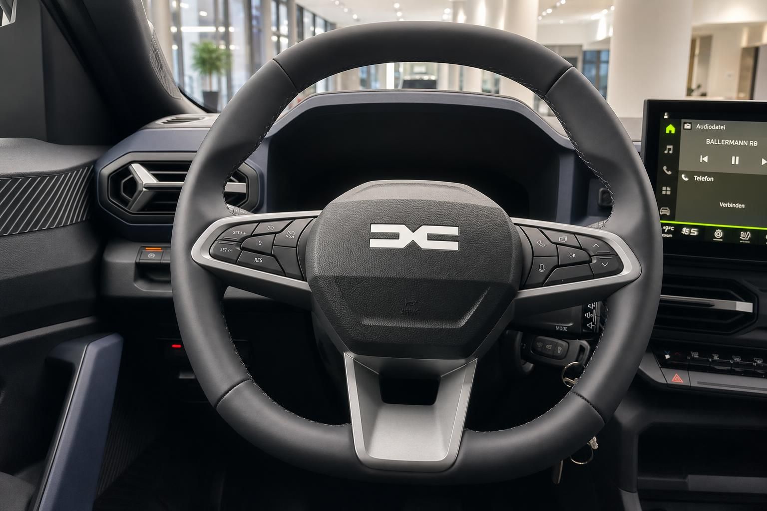 Dacia Lenkrad mit Logo und Multifunktionstasten sowie Infotainment-Display im Hintergrund