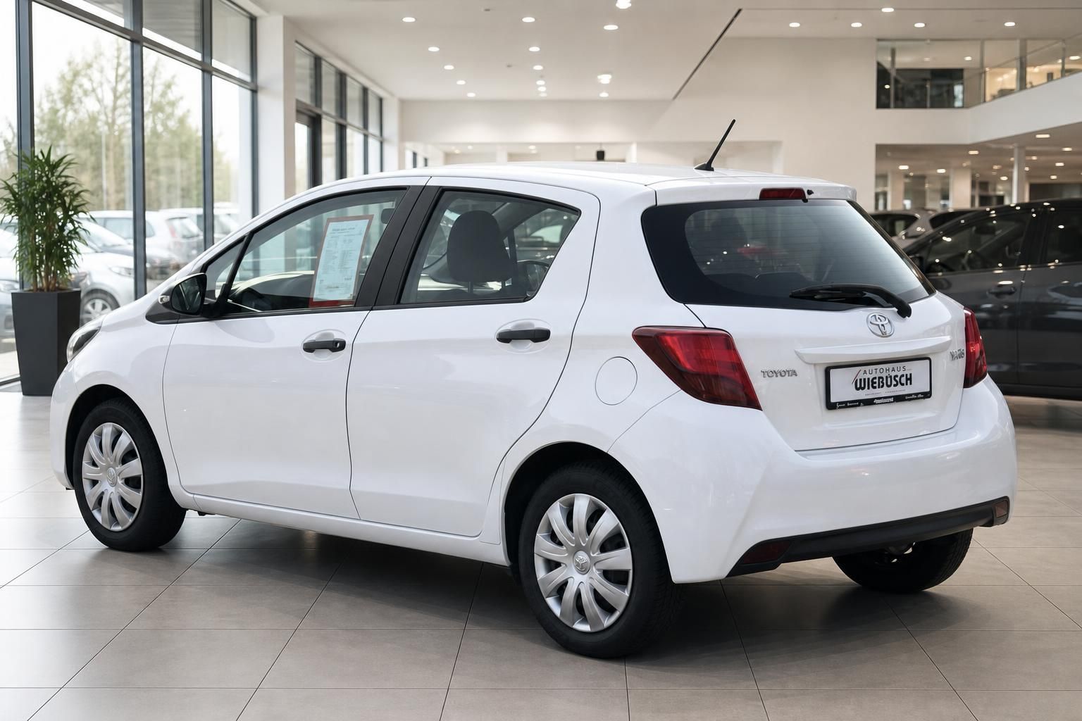 Weißer Toyota Yaris im Autohaus-Showroom - Rückansicht mit Händlerkennzeichen