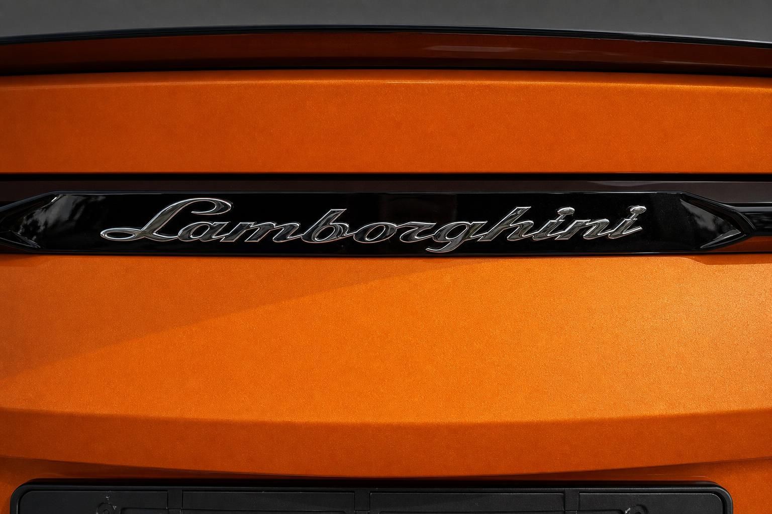 Lamborghini Schriftzug am Heck eines orangefarbenen Urus im Detail