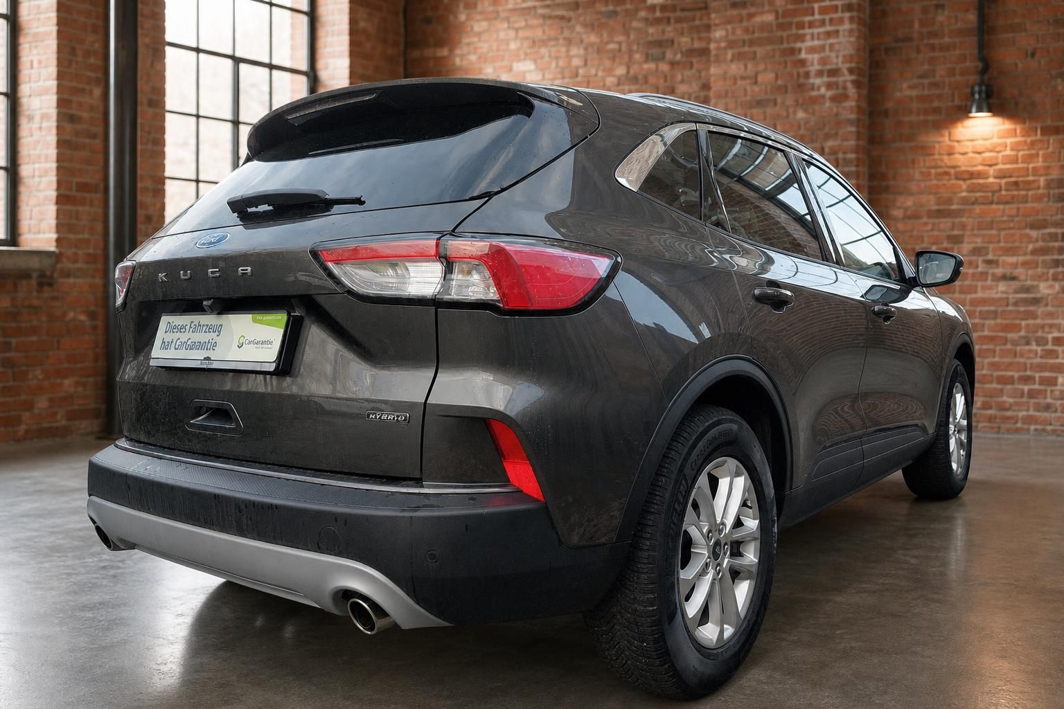 Ford Kuga Hybrid dunkelgrau Heckansicht schraeg in Backstein-Ambiente