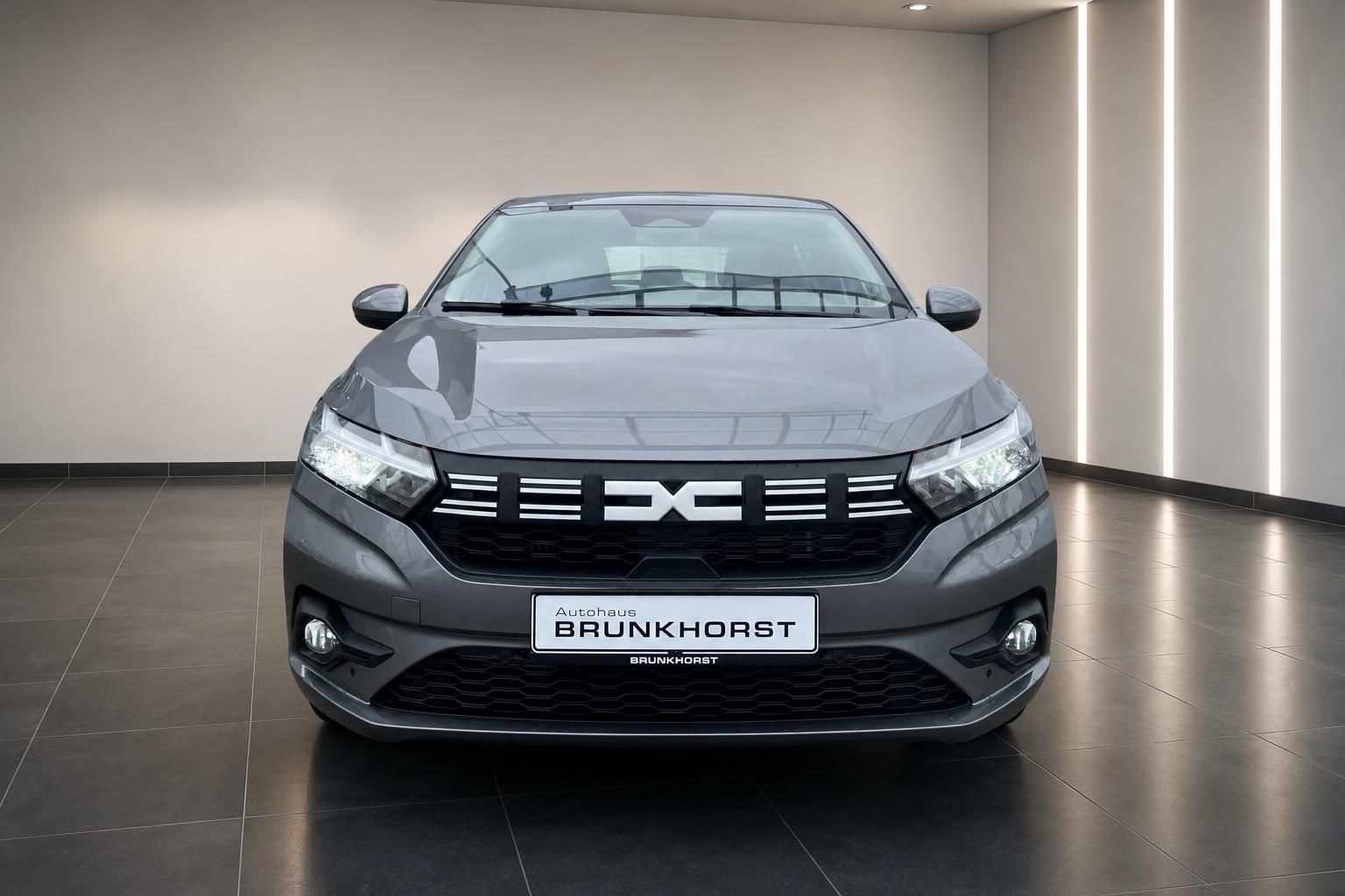 Dacia Frontansicht grau mit DC Logo-Kühlergrill im modernen Autohaus-Showroom