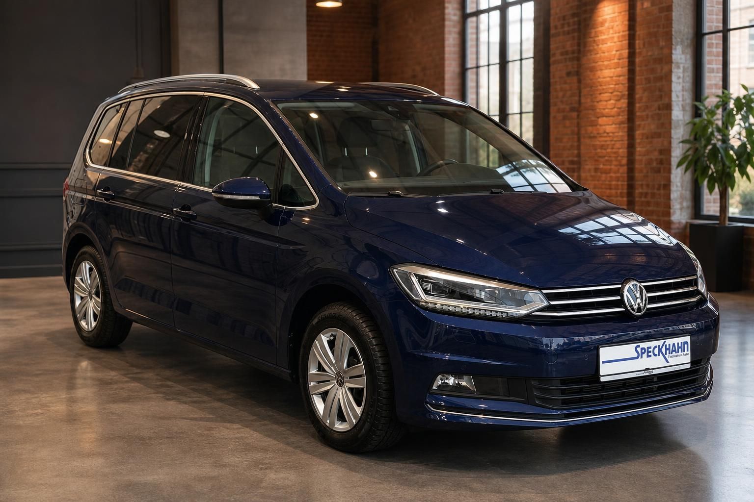 VW Touran blau metallic Frontansicht schräg vor Ziegelwand