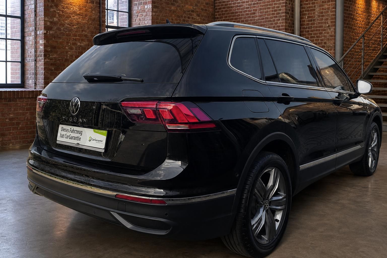 VW Tiguan schwarz Heckansicht in moderner Halle mit Backsteinwand