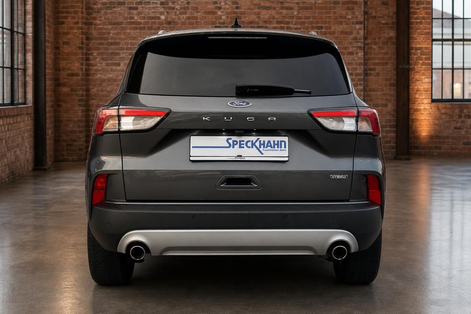 Ford Kuga Hybrid grau Heckansicht in Loftgebaeude mit Backsteinwand