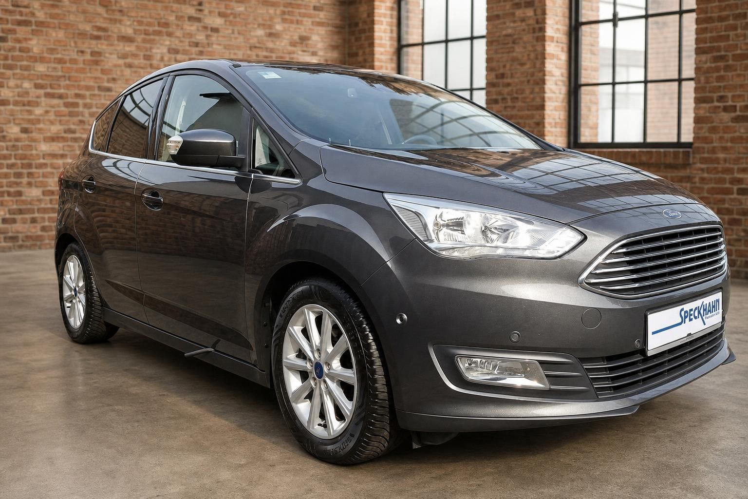 Ford C-MAX in Grau, Frontansicht schraeg vor Ziegelwand