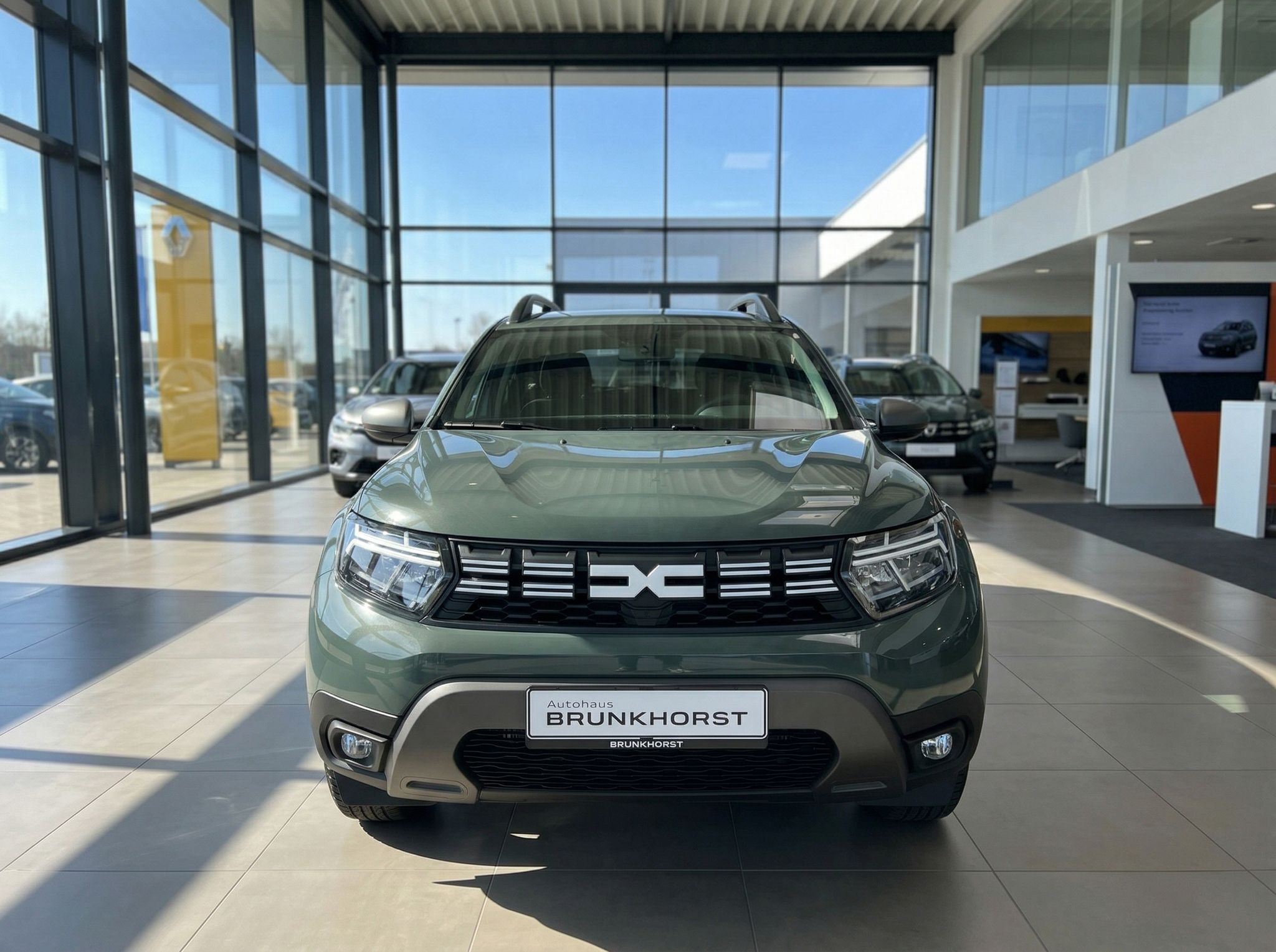 Dacia Duster grün metallic Frontansicht mit DC Logo im Autohaus Showroom